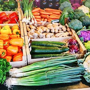 An in-store produce display with scallions; orange, yellow, red, and green peppers; carrots; ginger; eggplant; broccoli; purple cauliflower