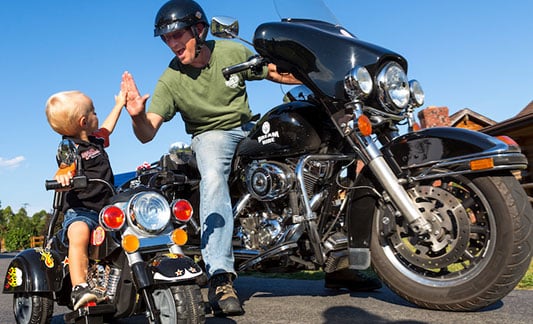 Guy on motorcycle high-fiving kid on 4 wheeled motorcycle