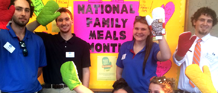 volunteers holding oven mitts in front of national family meals month sign