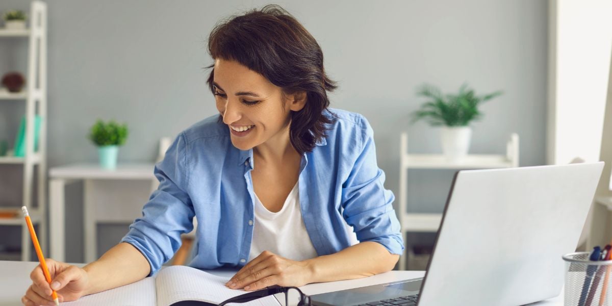 a woman takes notes during an online course