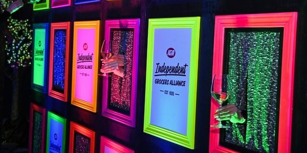 hands holding wine peek out of picture frames next to Independent Grocers Alliance logos