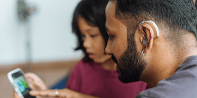 Person with hearing aid looks at phone with child