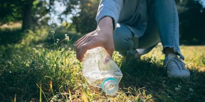 Person picks up a plastic bottle in the grass
