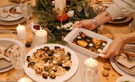 a holiday food spread on the table, with asparagus, tomatoes, and cheese, plus a roasted cauliflower dish